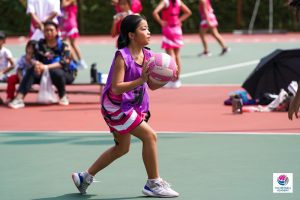 Young girl in a pink sports uniform holding a netball on an outdoor court.