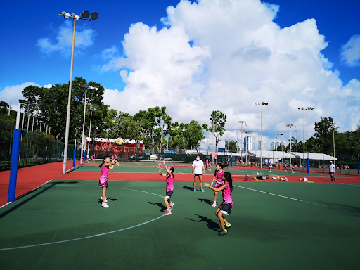 Young Singapore netball player balancing school books and a netball, illustrating student athlete demands